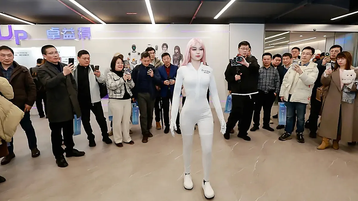 Human-like robot standing still in front of a crowd of people taking pictures.