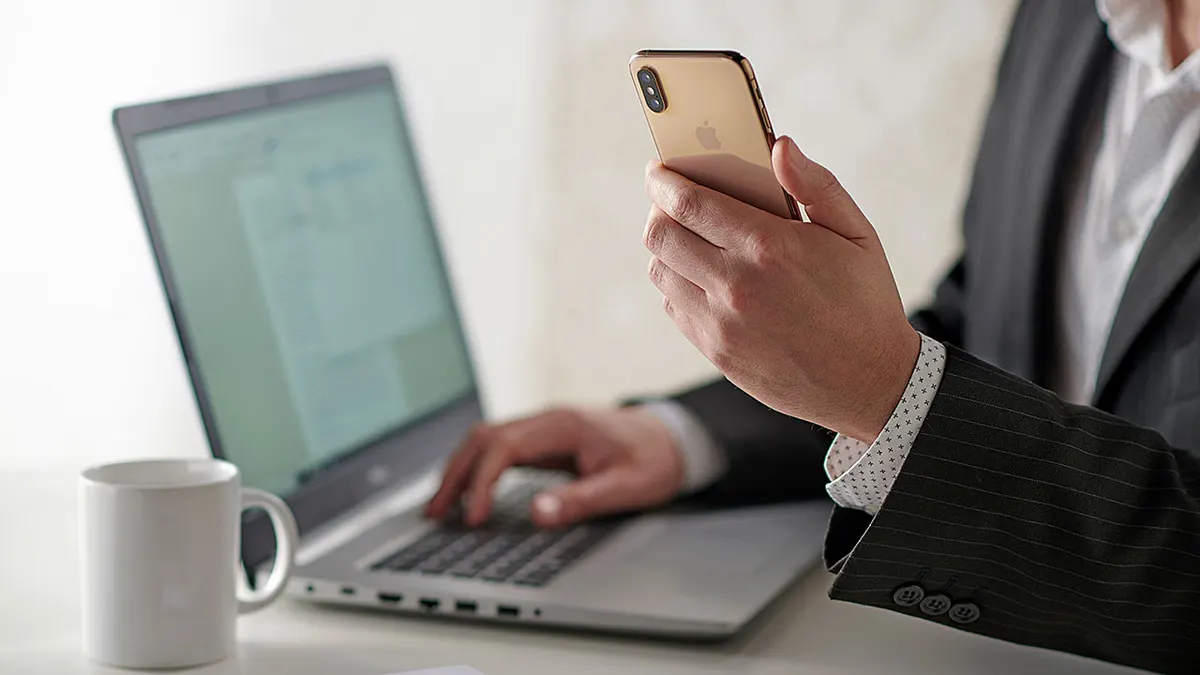 Man holding phone while typing on computer.