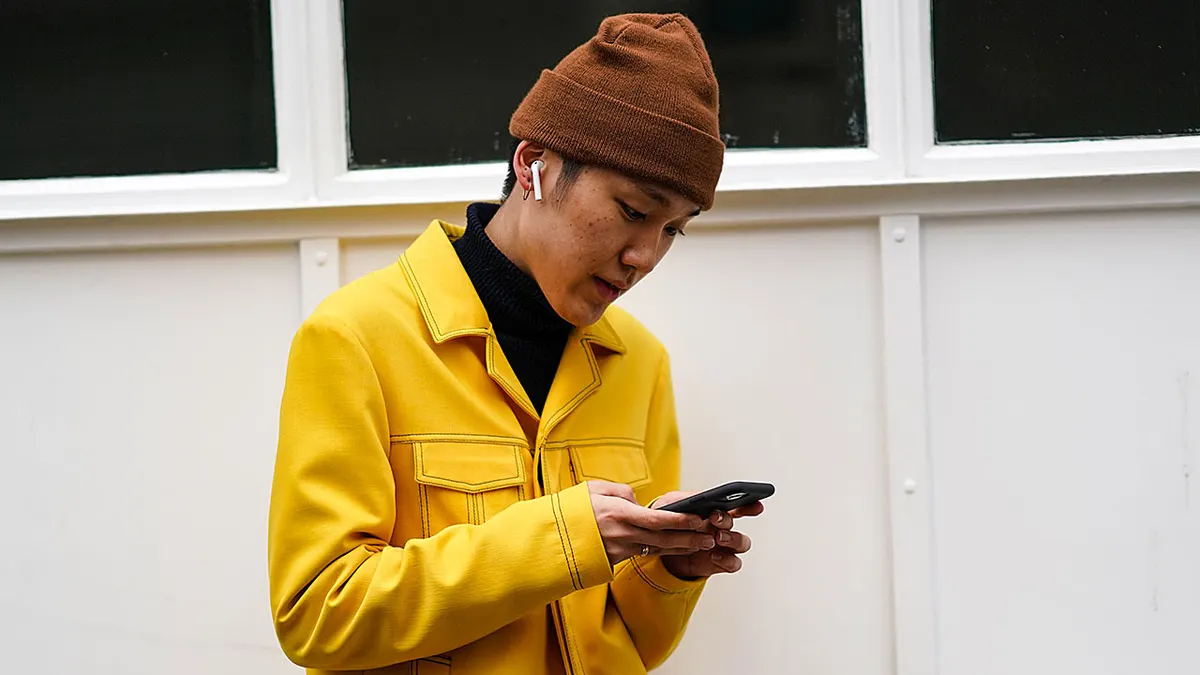 Man outside with Airpods looking at his phone.